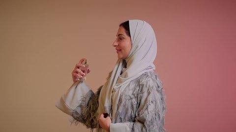 التطيب والتعطر بالعود العطري، التسويق للعطور والزيوت الطبيعية العالمية، عطورات عربية خليجية، سيدة اماراتية تسوق للمنتجات العطرية، تصوير مقرب لإمرأه عربيه سعودية محجبة ترتدي العباءة تقوم برش العطر، خلفية ملونة