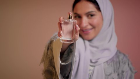 التسويق للعطور والزيوت الطبيعية العالمية، عطورات عربية خليجية، سيدة اماراتية تسوق للمنتجات العطرية، تصوير مقرب لإمرأه عربيه سعودية محجبة ترتدي العباءة تقوم برش العطر، التطيب والتعطر بالعود العطري، خلفية ملونة