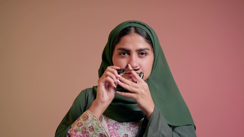 الشغف بوضع الميك اب، الاهتمام بالجمال والمظهر الخارجي, الترويج لمنتجات ومستحضرات التجميل, مفهوم التزين والتجمل, تصوير مقرب لامرأة عربية خليجية إماراتية محجبة ترتدي العباءة تقوم باستخدام المسكرة, شابة سعودية تضع المكياج, خلفية ملونة