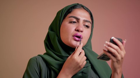 مفهوم التزين والتجمل, الترويج لمنتجات و مساحيق التجميل, استعمال المستحضرات التجميلية, العناية بالجمال والمظهر الخارجي, تصوير مقرب لامرأة عربية خليجية إماراتية محجبة ترتدي العباءة تضع أحمر شفاه, شابة سعودية تقوم بوضع المكياج, خلفية ملونة