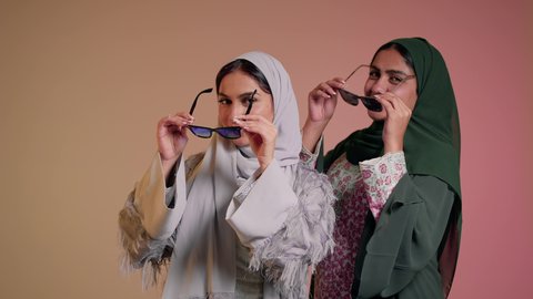 عرض إعلاني تسويقي، مواكبة أحدث صيحات الموضة والأزياء، الأناقة والاهتمام بالظهر الخارجي، بورتريه مقرب لسيدتين عربيتين خليجيتين سعوديتين ترتديان العباءة ونظاره شمسيه ملونه، صديقتان امراتيتان محجبتان تنظران إلى الكاميرا بإيماءات الانوثه والدلع والدلال، خلفية ملونة