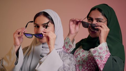 الأناقة والاهتمام بالظهر الخارجي، عرض إعلاني تسويقي، مواكبة أحدث صيحات الموضة والأزياء، بورتريه مقرب لسيدتين عربيتين خليجيتين سعوديتين ترتديان العباءة ونظاره شمسيه ملونه، صديقتان امراتيتان محجبتان تنظران إلى الكاميرا بإيماءات الانوثه والدلع والدلال، خلفية ملونة