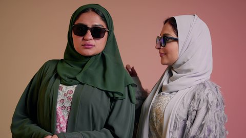 عرض إعلاني تسويقي، مواكبة أحدث صيحات الموضة والأزياء، الأناقة والاهتمام بالظهر الخارجي، بورتريه مقرب لسيدتين عربيتين خليجيتين سعوديتين ترتديان العباءة ونظاره شمسيه ملونه، صديقتان امراتيتان محجبتان تنظران إلى الكاميرا بإيماءات الانوثه والدلع والدلال، خلفية ملونة