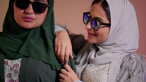 التسويق لماركة ومنتج محلي، الاهتمام بالمظهر الخارجي، مواكبة أحدث صيحات الموضة والأزياء، بورتريه مقرب لسيدتين عربيتين خليجيتين سعوديتين ترتديان العباءة ونظاره شمسيه ملونه، صديقتان امراتيتان محجبتان تنظران إلى الكاميرا بإيماءات الانوثه والدلع والدلال، خلفية ملونة