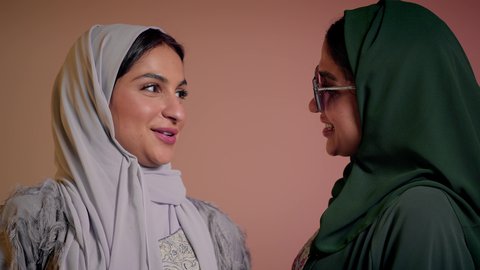 إيماءات الانوثه والدلع والدلال، متابعة أحدث صيحات الموضة، التسويق لماركة ومنتج محلي، بورتريه مقرب لسيدتين عربيتين خليجيتين سعوديتين ترتديان العباءة ونظاره شمسيه ملونه، صديقتان امراتيتان محجبتان تقومان تبادل الأحاديث بتعابير السعادة، خلفية وردية
