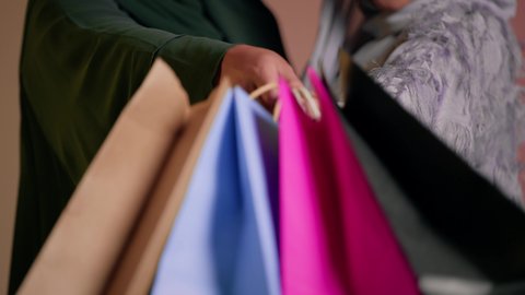 Buying gifts and necessities, enjoying shopping with friends, taking advantage of offers and discounts, looking at the camera with happy gestures, close-up portrait of two Saudi Arabian Gulf women wearing abaya, two veiled female friends holding paper bags, pink background