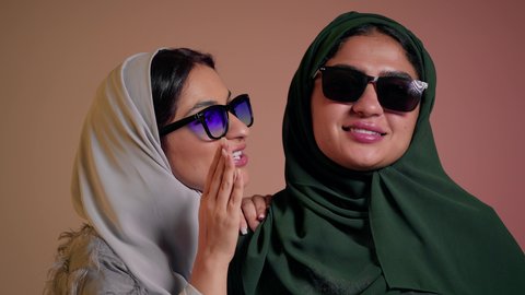Laughter and fun with friends, elegance and interest in appearance, following the latest fashion trends, close-up portrait of two Saudi Arabian Gulf women wearing abaya and colored sunglasses, two veiled female friends looking at something with gestures of happiness and fun, colorful background