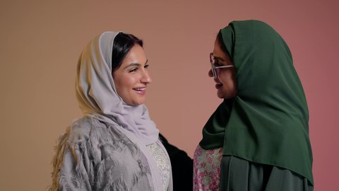 إظهار مشاعر الحب والشغاف، قضاء وقت ممتع مع الاصدقاء، النظر إلى الكاميرا بتعابير السعادة، الأناقة والاهتمام بالمظهر الخارجي، امرأة اماراتية تضع النظارة الشمسية، بورتريه لصديقتين عربيتين خليجيتين سعوديتين ترتديان العباءة تقومان بتشكيل اليدين على شكل قلب، خلفية وردية