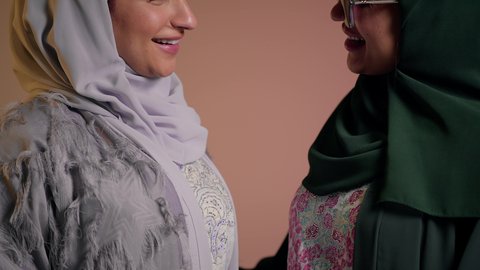 قضاء وقت ممتع مع الاصدقاء، إظهار مشاعر الحب والشغاف، النظر إلى الكاميرا بتعابير السعادة، امرأة اماراتية تضع النظارة الشمسية، بورتريه مقرب لصديقتين عربيتين خليجيتين سعوديتين ترتديان العباءة تقومان بتشكيل اليدين على شكل قلب، خلفية وردية