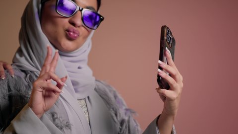 إيماءات  الانوثه والدلع والدلال، استخدام احدث التقنيات الحديثه، تصوير مقرب لسيدتين عربيتين خليجيتين سعوديتين ترتديان نظاره شمسيه ملونه، صديقتان عربيتان خليجيتان امراتيتان ترتديان العباءه تقومان بالتقاط صور سيلفي تذكاريه عبر الهاتف المحمول، خلفية ملونة