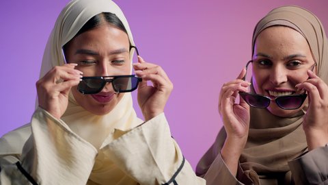 إبراز الجمال الاماراتي، مفهوم الاهتمام بالأناقة والمظهر الخارجي، بورترية مقرب لصديقتان عربيتان خليجيتان اماراتيان تقومان بوضع النظارة الشمسية، سيدتان سعوديتان تنظران الى الكاميرا بايماءات الثقه و الاعتزاز بالنفس ، خلفية ملونه