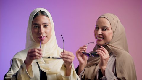 مفهوم الاهتمام بالأناقة والمظهر الخارجي، بورترية مقرب لصديقتان عربيتان خليجيتان اماراتيان تقومان بوضع النظارة الشمسية، سيدتان سعوديتان تنظران الى الكاميرا بايماءات الثقه و الاعتزاز بالنفس، ، خلفية ملونه