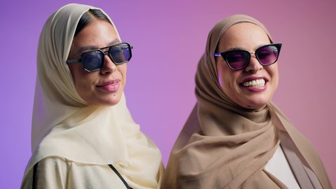مفهوم النعومة والانوثة، الاعتزاز و الثقه بالنفس، بورترية مقرب لصديقتان عربيتان خليجيتان اماراتيان ترتديان العباءة الملونه و النظارات الشمسية، سيدتان سعوديتان تنظران الى الكاميرا بايماءات السعادة و السرور ، خلفية ملونه