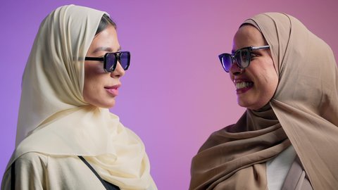 الحب و المودة بين الأشقاء، الاعتزاز و الثقه بالنفس، بورترية مقرب لصديقتان عربيتان خليجيتان اماراتيان ترتديان العباءة الملونه و النظارات الشمسية، سيدتان سعوديتان تنظران الى الكاميرا بايماءات السعادة و السرور ، خلفية ملونه