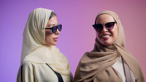 Pride and self-confidence, close-up portrait of two Emirati Gulf Arab friends wearing colorful abaya and sunglasses, two Saudi women looking at the camera with gestures of happiness and pleasure, colorful background