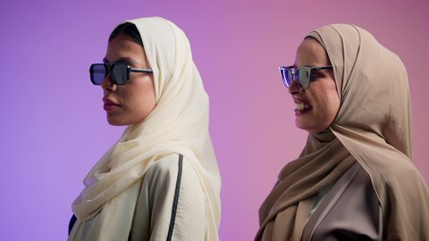 مفهوم الموضة والأناقة، الاهتمام بالجمال والمظهر الخارجي، بورترية مقرب لصديقتان عربيتان خليجيتان اماراتيان ترتديان العباءة الملونه و النظارات الشمسية، سيدتان سعوديتان تنظران الى الكاميرا بايماءات الثقه و الاعتزاز بالنفس، ، خلفية ملونه