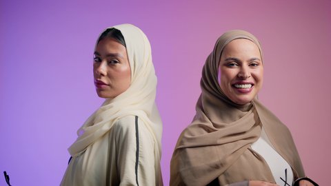 The concept of softness and femininity, interest in beauty and outward appearance, a close-up portrait of two Arab Gulf Emirati friends wearing sunglasses, two Saudi women looking at the camera with gestures of confidence and self-esteem, a colorful background