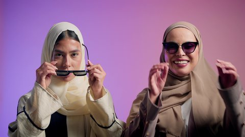 مفهوم العناية بالمظهر الخارجي، الاهتمام بالموضة والأناقة، بورترية لصديقتان عربيتان خليجيتان اماراتيان تقومان بوضع النظارة الشمسية، سيدتان سعوديتان تقومان بالنظر الى الكاميرا بايماءات الثقه و الاعتزاز بالنفس، ، خلفية ملونه