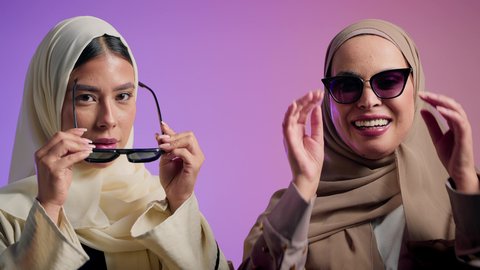 مفهوم العناية بالجمال والإطلالة المتميزة، الاهتمام بالأناقة والمظهر الخارجي، بورترية لصديقتان عربيتان خليجيتان اماراتيان تقومان بوضع النظارة الشمسية، سيدتان سعوديتان تقومان بالنظر الى الكاميرا بايماءات الثقه و الاعتزاز بالنفس، ، خلفية ملونه