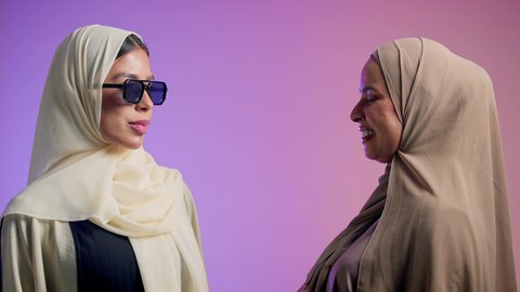 مفهوم الأناقة والأنوثة، الموضة والأناقة والاهتمام بالمظهر الخارجي، بورترية مقرب لشابتان عربيتان خليجتان اماراتيان محجبتان مبتسمتان ترتديان العباءة الملونه تنظران إلى الكاميرا بإيماءات السرور والثقة بالنفس ، عباءات خليجية نسائية عصرية،خلفية ملونه