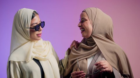 أزياء عصرية راقية، مفهوم النعومة والشياكة والأنوثة، الموضة والأناقة والاهتمام بالمظهر الخارجي، بورترية مقرب لشابتان عربيتان خليجتان سعوديتان محجبتان مبتسمتان ترتديان العباءة الملونه تنظران إلى الكاميرا بإيماءات السرور والثقة بالنفس، صديقتان اماراتيان يقومان بقضاء أوقات ممتعة ، خلفية ملونه