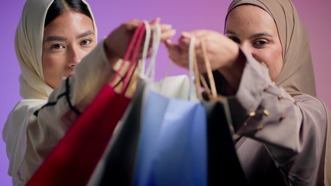 عروض الجمعه البيضاء، شراء الهدايا والمستلزمات الشخصيه ، استغلال التخفيضات والعروض المشوقه، بورتريه مقرب ليد سيدتان عربيتان خليجيتان سعوديتان ترتديان الحجاب والعباءه الملونه تحملان أكياس التسوق ، صديقتان اماراتيان تقومان بالاستمتاع بالشراء من المولات والمحال التجاريه، خلفيه ملونه