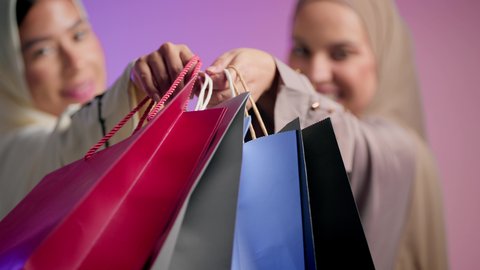 Buying gifts and personal supplies, taking advantage of discounts and exciting offers, close-up portrait of two Saudi Arabian Gulf women wearing colorful hijab and abaya carrying shopping bags, two Emirati friends enjoying shopping in malls and shops, White Friday offers, colorful background