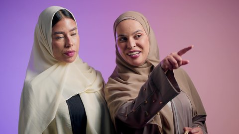إيماءات وتعابير وجه تدل على رؤية شيء جميل،  بناء علاقات اجتماعية ناجحة بين الأشخاص، بورترية مقرب لسيده عربيه خليجيه اماراتية تقوم بالاشارة الى شيء ما برفقه صديقتها ،شابتان سعوديتان محجبتان يقومان بقضاء اوقات ممتعه ، خلفية ملونة