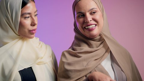Gestures of happiness and pleasure, building successful social relationships between people, close-up portrait of an Arab Gulf Emirati woman pointing at something with her friend, two veiled Saudi girls having a good time, colorful background
