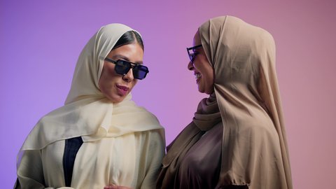 الاهتمام بالمظهر الخارجي و الأناقة، مفهوم الثقة بالنفس، الحب والمودة بين الاصدقاء، بورترية مقرب لإمرأة عربية خليجية اماراتية ترتدي الحجاب والعباءة الملونه برفقه صديقتها تنظر الى الكاميرا بإيماءات السعادة ، شابتان سعوديتان ترتديان النظارات الشمسية تقضيان أوقات ممتعة ومسلية، خلفية ملونه