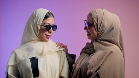 مفهوم الثقة بالنفس، العلاقة الاخوية الايجابية، الحب والمودة بين الاصدقاء، بورترية مقرب لإمرأة عربية خليجية اماراتية ترتدي الحجاب والعباءة الملونه برفقه صديقتها تنظر الى الكاميرا بإيماءات السعادة ، شابتان سعوديتان ترتديان النظارات الشمسية تقضيان أوقات ممتعة ومسلية، خلفية ملونه