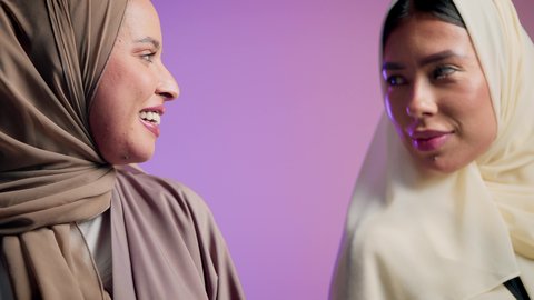 مفهوم الموضة والأناقة والاهتمام بالمظهر الخارجي، بورترية مقرب لشابتان عربيتان خليجتان اماراتيان محجبتان مبتسمتان ترتديان العباءة الملونه تنظران إلى الكاميرا بإيماءات السرور والثقة بالنفس ، النعومة والشياكة والأنوثة، عباءات خليجية نسائية عصرية، خلفية ملونه