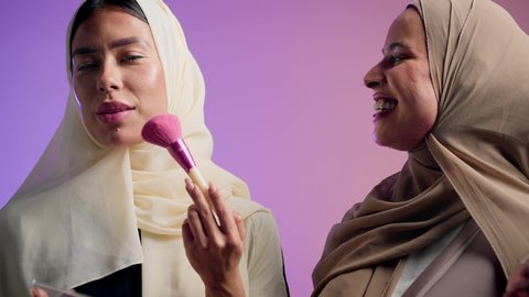 الاهتمام والعناية بالمظهر الخارجي, استخدام المساحيق التجميلية, بورتريه مقرب لصديقتان عربيتان خليجيتان اماراتيان يقومان بالتزين و التجمل, الأنوثة والاهتمام بالجمال، خلفية ملونه