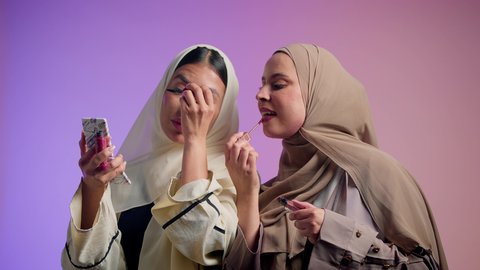 الشغف بوضع أحمر الشفاه، مستحضرات نسائيه عالميه، مفهوم الأناقة والإهتمام بالمظهر الخارجي، بورتريه لصديقتان عربيتان اماراتيان خليجيتان تستمتعان بالتزيين النسائي, رسم العيون بأستخدام الماسكرا، خلفية ملونة