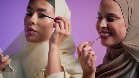 استخدام الايلاينر لإبراز جمال العينين، مستحضرات نسائيه عالميه، مفهوم الأناقة والإهتمام بالمظهر الخارجي، بورتريه مقرب لصديقتان عربيتان اماراتيان خليجيتان تستمتعان بالتزيين النسائي، الشغف بوضع أحمر الشفاه، خلفية ملونة