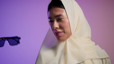 Enjoying modern accessories, the concept of fashion and elegance, an Emirati woman wearing an elegant abaya and contemporary black sunglasses, a photograph of a veiled Saudi Arabian Gulf woman trying on new sunglasses, attention to one's appearance, gestures of femininity and beauty, a colorful background.