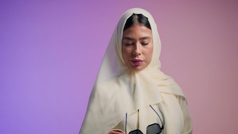 سيدة اماراتية ترتدي عباءة أنيقة ونظارة سوداء معاصرة،  تصوير لإمرأة عربية خليجية سعودية محجبة تقوم بتجربة النظارات الشمسية الجديدة، مفهوم الموضة والاناقة ، الاهتمام بالمظهر الخارجي ، إيماءات الانوثة والجمال, خلفية ملونة
