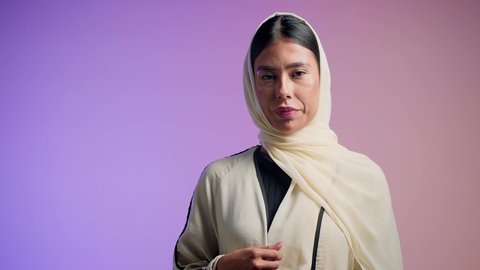 التعطر والتطيب بالعود والزيوت العطرية,  سيدة اماراتية تستخدم المستحضرات النسائية, التسويق لمنتجات العطور ، تصوير مقرب لامرأة عربيه سعودية خليجية محجبة مبتسمة تمسك بيدها زجاجة وتقوم برش العطر، خلفية ملونة