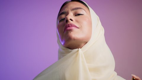 An Emirati woman using feminine products, perfuming and applying oud and essential oils, marketing perfume products. A close-up photograph of a smiling veiled Saudi Arabian Gulf woman holding a bottle and spraying perfume, a colorful background.