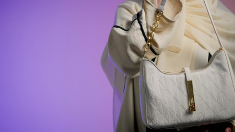 تصوير مقرب ليد شابة عربية سعودية خليجية محجبة تحمل بيدها حقيبة بإيماءات السعادة ، سيدة اماراتية ترتدي العباءة الخليجية العصرية ،مفهوم الموضة والأناقة، أزياء واكسسوارات نسائيه ، عرض موديلات حقائب عالمية فاخرة