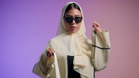 أزياء واكسسوارات نسائيه ، عرض موديلات حقائب عالمية فاخرة، سيدة اماراتية ترتدي العباءة الخليجية العصرية ونظارة شمسية سوداء، مفهوم الموضة والأناقة، تصوير مقرب لشابة عربية سعودية خليجية محجبة تحمل بيدها حقيبة بإيماءات السعادة