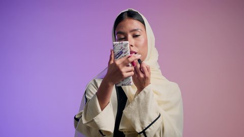 Passion for applying lipstick. Global women's products. The concept of elegance and interest in appearance. A photograph of a veiled Saudi Arabian Gulf woman enjoying feminine adornment. An Emirati woman wearing an elegant abaya and using cosmetics. A colorful background.