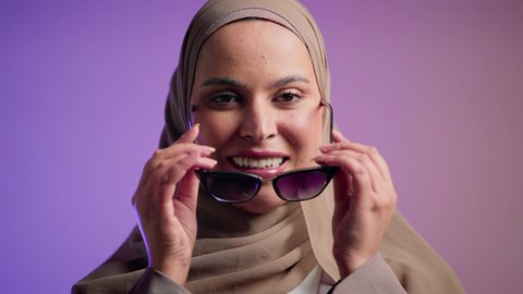 تعابير السرور والسعادة ، الاستمتاع بإمتلاك اكسسوارات عصرية,  الاهتمام بالمظهر الخارجي والاناقه ،سيدة اماراتية ترتدي عباءة أنيقة ونظارة سوداء معاصرة, إيماءات الانوثة والجمال, تصوير لإمرأة عربية خليجية سعودية محجبة تقوم بتجربة النظارات الشمسية الجديدة,  خلفية ملونة