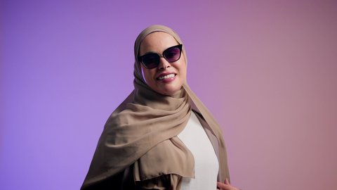 Expressions of joy and happiness, an Emirati woman wearing an elegant abaya and contemporary black sunglasses, enjoying owning modern accessories, gestures of femininity and beauty, interest in appearance and elegance, a photograph of a veiled Saudi Arabian Gulf woman trying on new sunglasses, colorful background.