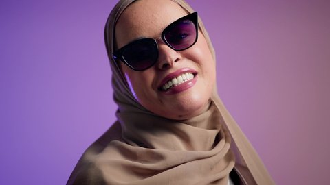 سيدة اماراتية ترتدي عباءة أنيقة ونظارة سوداء معاصرة, الاستمتاع بإمتلاك اكسسوارات عصرية,  إيماءات الانوثة والجمال, الاهتمام بالمظهر الخارجي والاناقه ، تصوير لإمرأة عربية خليجية سعودية محجبة تقوم بتجربة النظارات الشمسية الجديدة,  خلفية ملونة