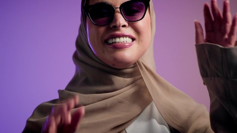 إيماءات الانوثة والجمال, الاهتمام بالمظهر الخارجي والاناقه ، تصويرلإمرأة عربية خليجية سعودية محجبة تقوم بتجربة النظارات الشمسية الجديدة,  سيدة اماراتية ترتدي عباءة أنيقة ونظارة سوداء معاصرة, الاستمتاع بإمتلاك اكسسوارات عصرية,  خلفية ملونة