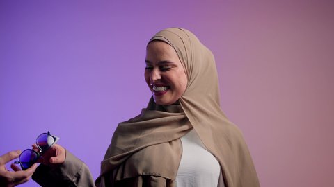 سيدة اماراتية ترتدي عباءة أنيقة ونظارة سوداء معاصرة, مفهوم الموضة والأناقة, الاستمتاع بإمتلاك اكسسوارات عصرية, تصوير لإمرأة عربية خليجية سعودية محجبة تقوم بتجربة النظارات الشمسية الجديدة, إيماءات الانوثة والجمال, خلفية ملونة