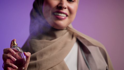 Emirati woman using feminine hygiene products, using oud and essential oils to perfume, marketing perfume products, close-up of a smiling veiled Saudi Arabian Gulf woman holding a bottle and spraying perfume, colorful background.