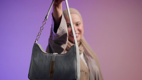 Display of luxury international handbag models, women's fashion and accessories, an Emirati woman wearing a modern Gulf abaya, the concept of fashion and elegance. A close-up of a veiled young Saudi Arabian Gulf woman holding a bag with a happy gesture.