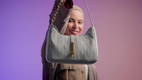 أزياء واكسسوارات نسائيه ، سيدة اماراتية ترتدي العباءة الخليجية العصرية ، مفهوم الموضة والأناقة، تصوير مقرب لشابة عربية سعودية خليجية محجبة تحمل بيدها حقيبة بإيماءات السعادة، عرض موديلات حقائب عالمية فاخرة